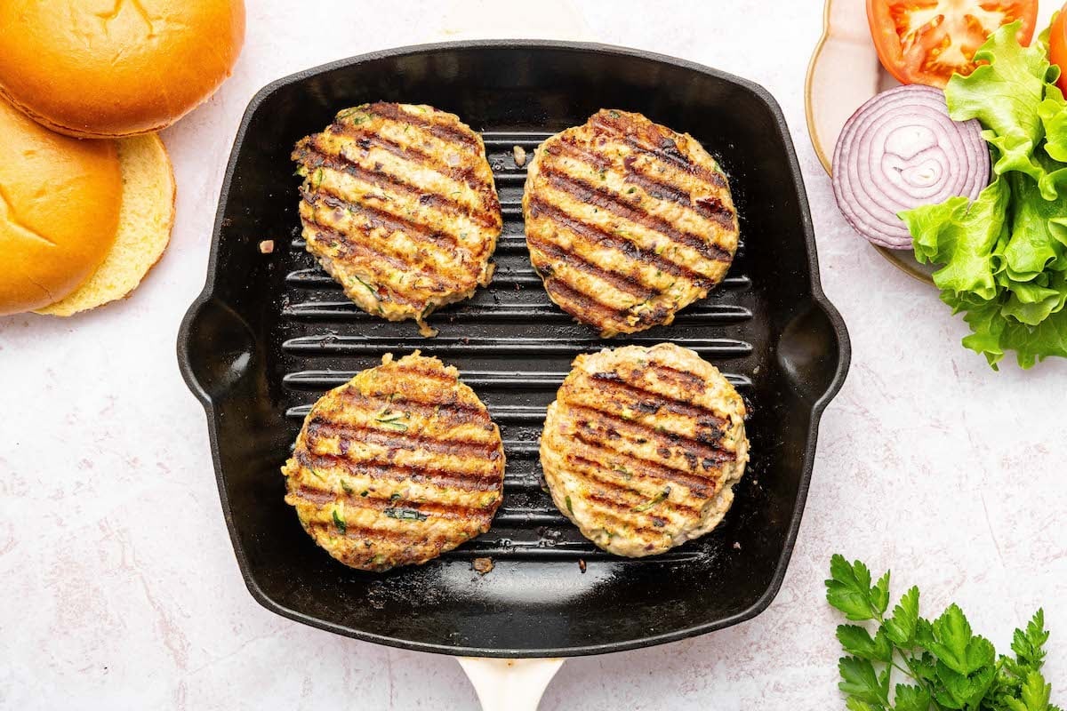 Four cooked ground chicken patties on a grill pan.