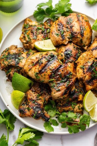 Cooked cilantro lime chicken thighs served on a plate topped with fresh cilantro and lime wedges.