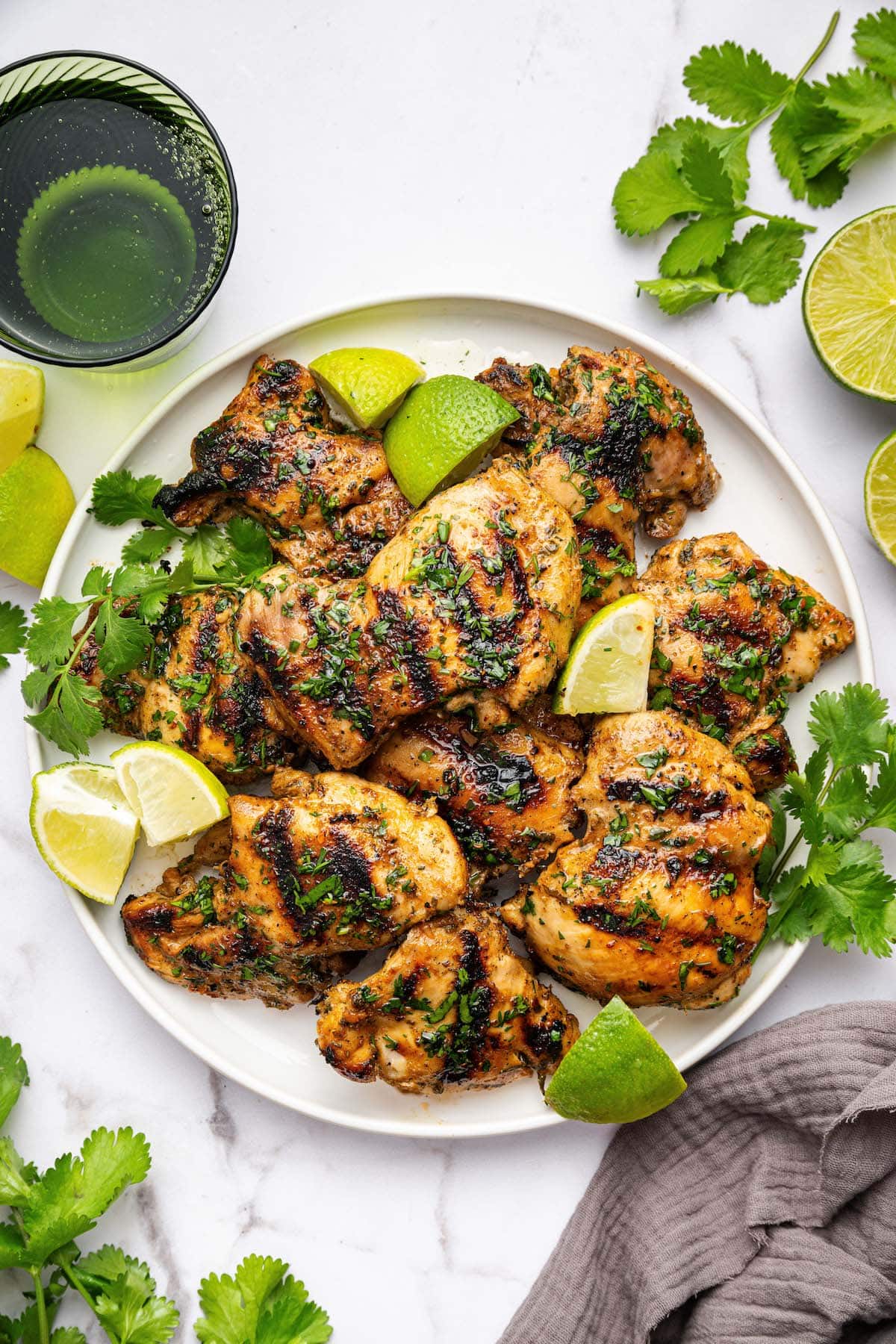 Cooked cilantro lime chicken thighs served on a plate topped with fresh cilantro and lime wedges.