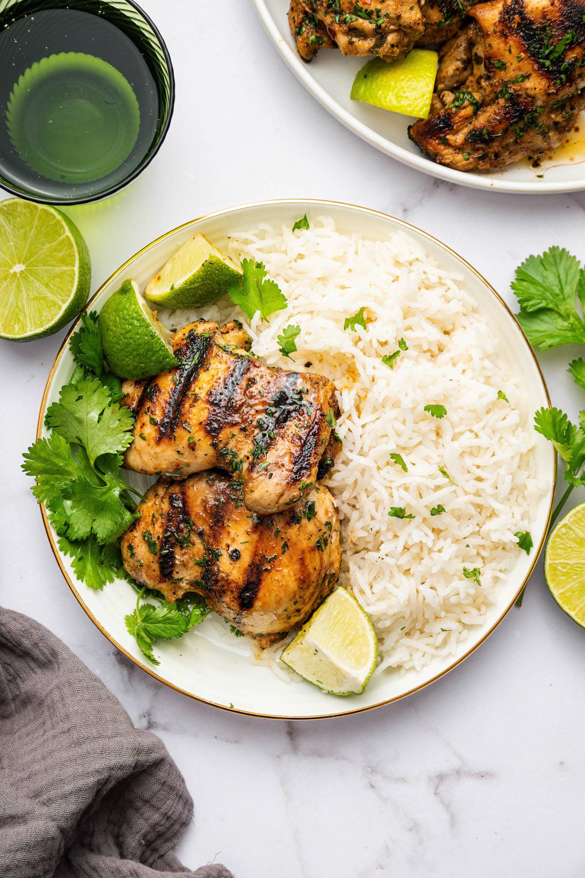 Two cilantro lime chicken thighs served on a plate with fresh cilantro, white rice and lime wedges.