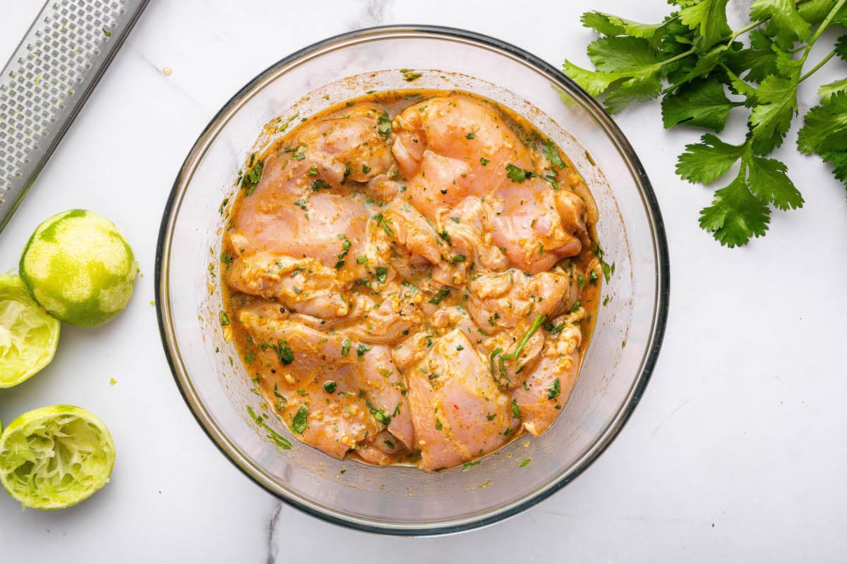 Raw chicken thighs marinating in a glass bowl with a cilantro lime marinade.