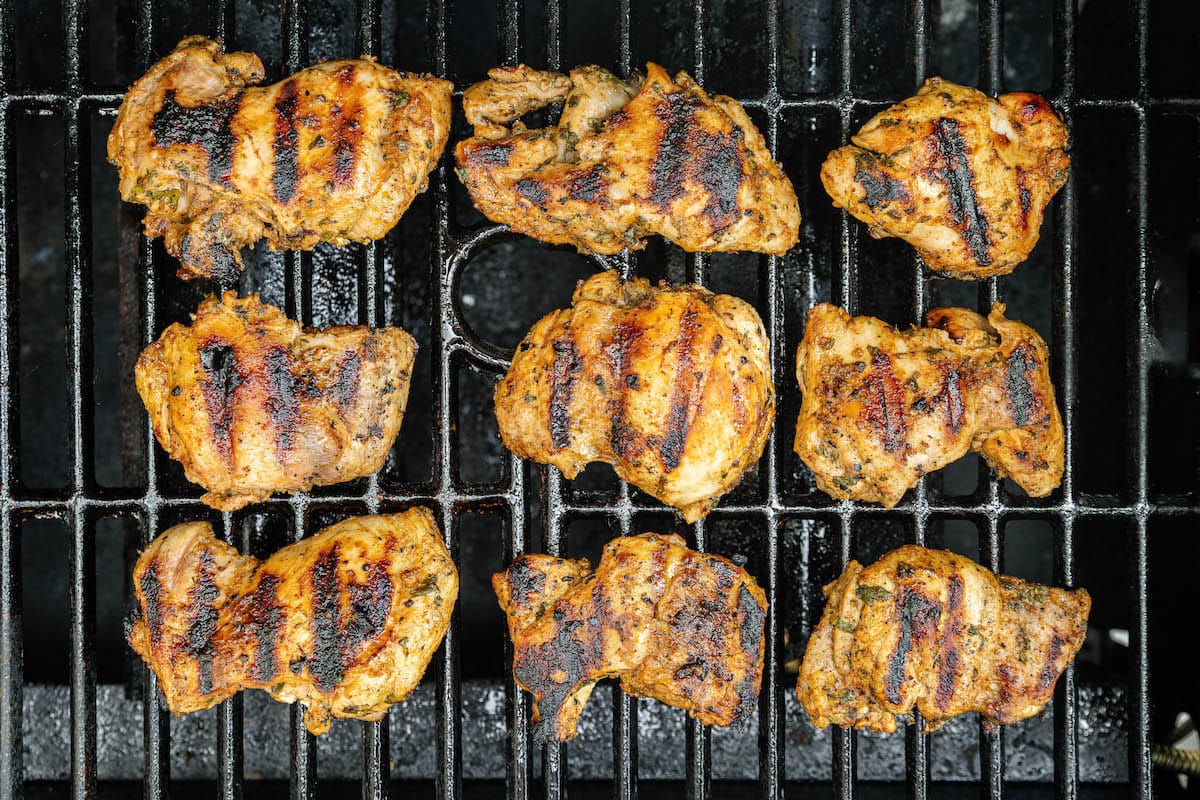 Nine cilantro lime chicken thighs cooking on a grill.