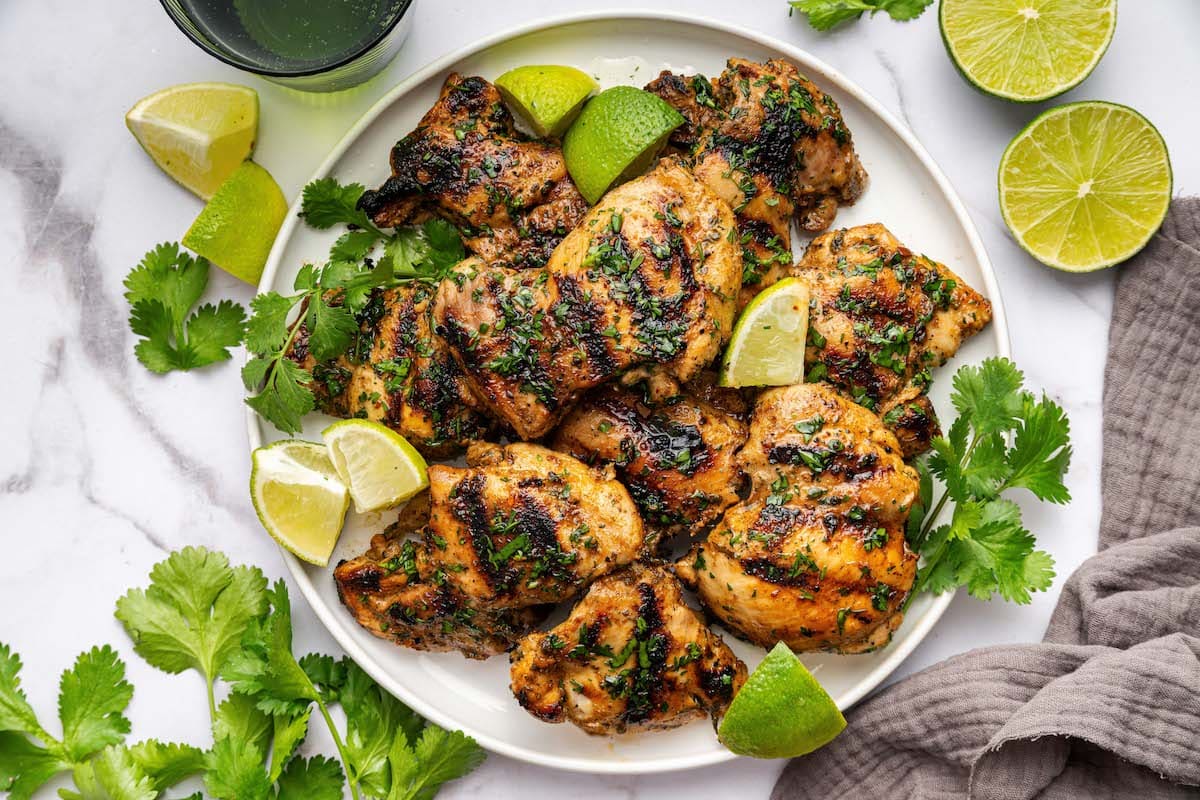 Cooked cilantro lime chicken thighs served on a plate topped with fresh cilantro and lime wedges.