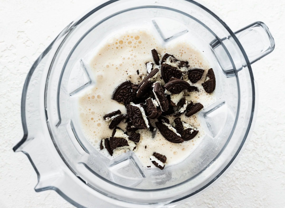 Crushed chocolate sandwich cookies added to a blender filled with a vanilla protein shake base, before blending into a cookies and cream shake.