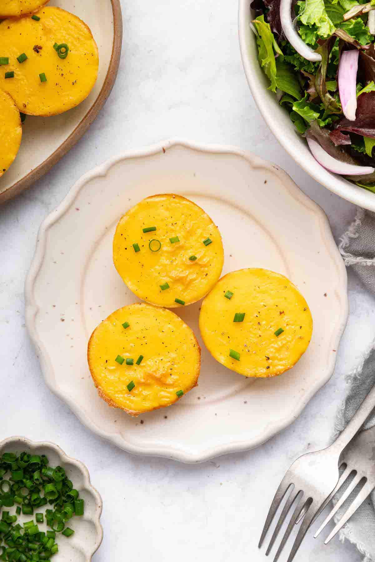 Three cottage cheese egg bites on a small white plate topped with chopped chives.