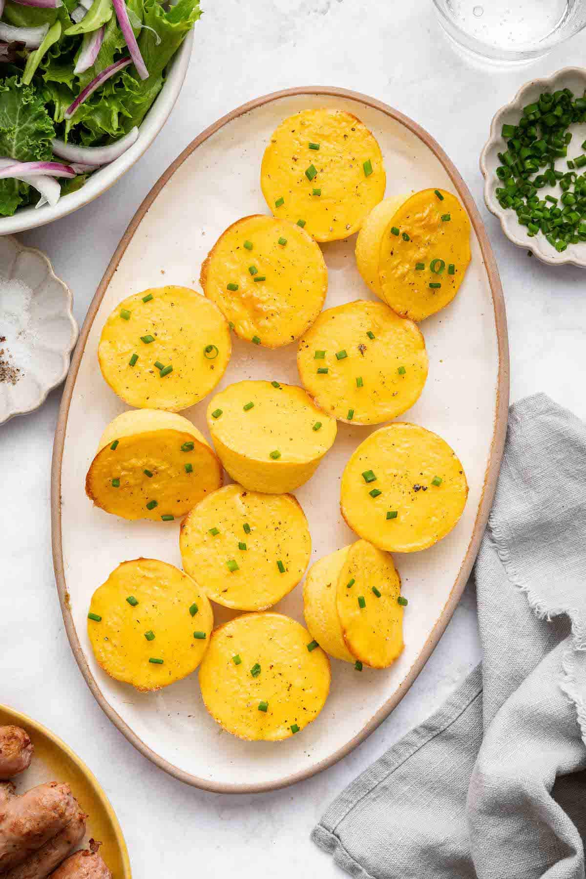 12 cottage cheese egg bites on a white serving plate topped with chopped chives. There is a salad next to the plate.