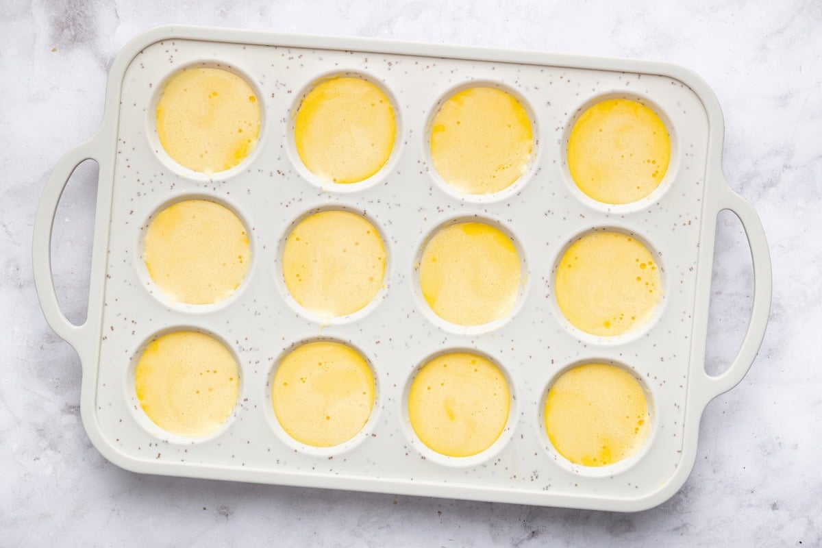 The cottage cheese egg bite mixture divided between 12 muffin cups in a silicone muffin tray.