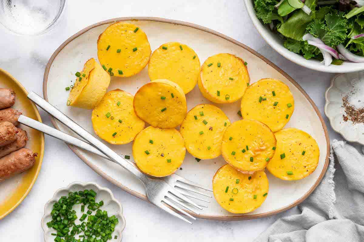 12 cottage cheese egg bites on a white serving plate topped with chopped chives. There are two forks on the plate.