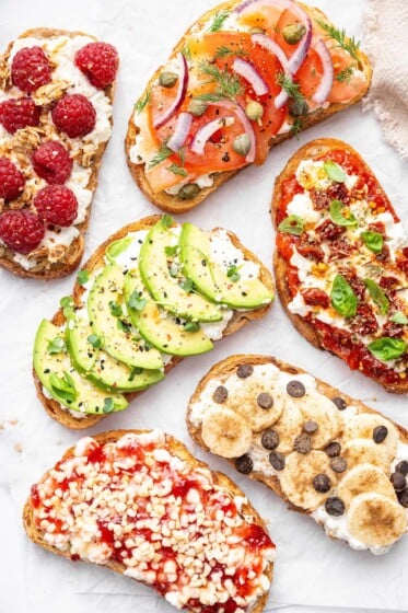 Assorted cottage cheese toast ideas topped with avocado, smoked salmon, pizza marinara, raspberries, banana with chocolate chips, and berry jam.