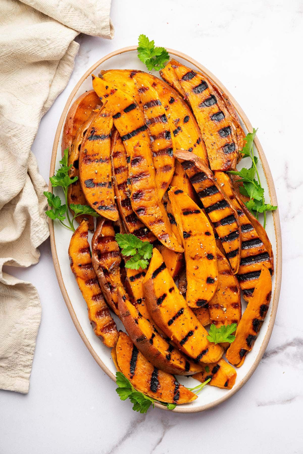 Grilled sweet potatoes on a serving platter topped with fresh parsley.