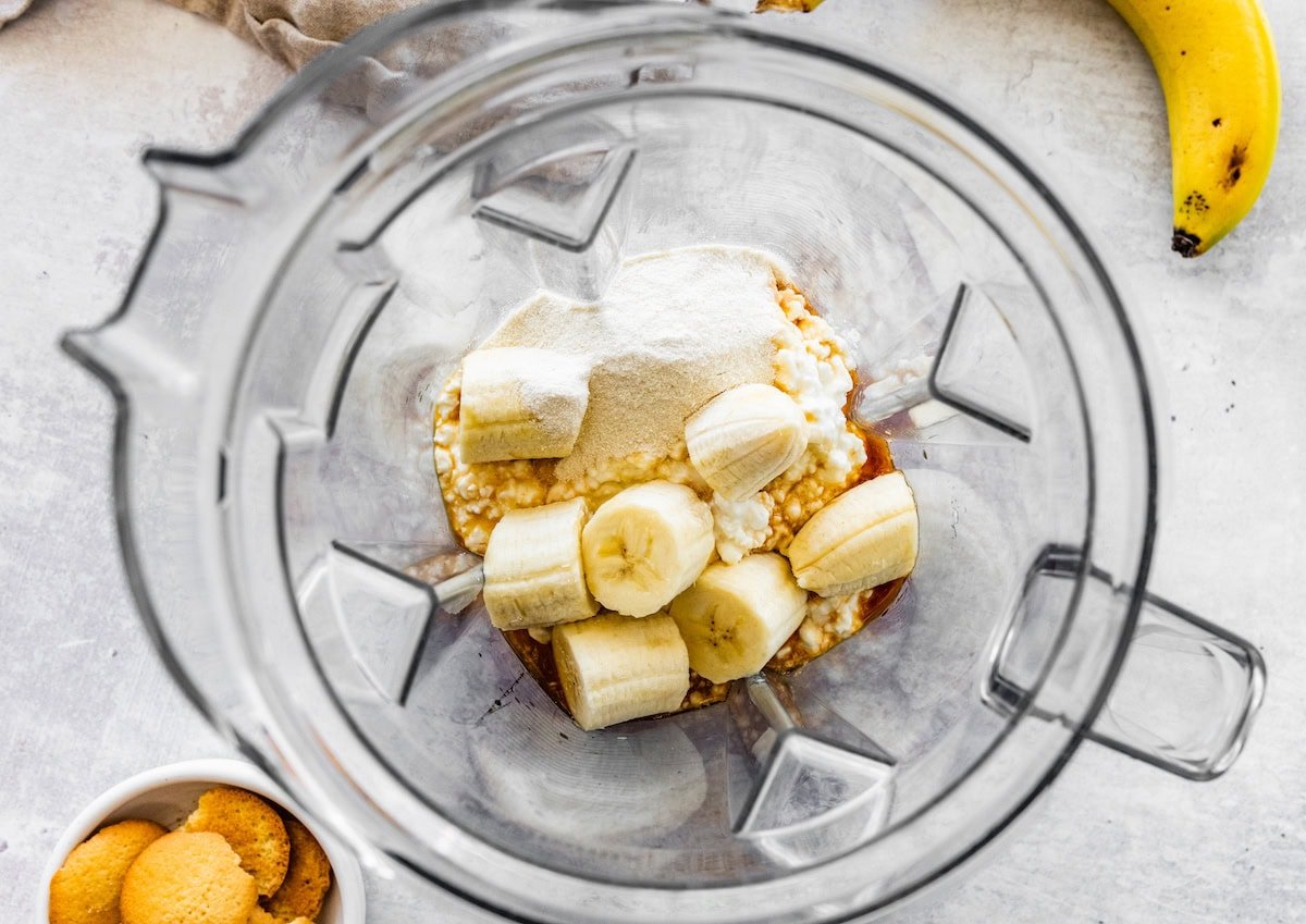 Ingredients for the high-protein banana pudding in the base of a blender: banana, cottage cheese, maple syrup, vanilla and protein powder.