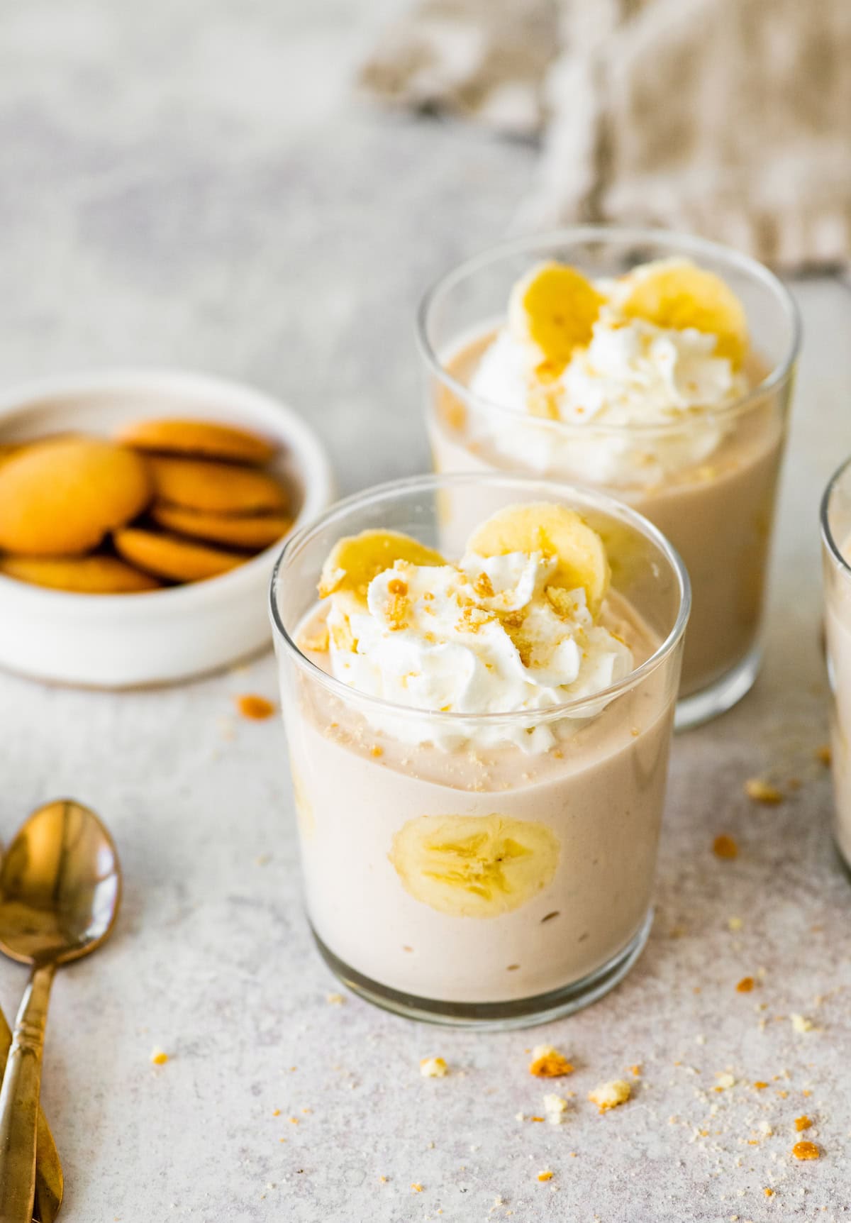 Two glasses filled the high-protein banana pudding topped with whipped cream, sliced bananas and crushed cookies.