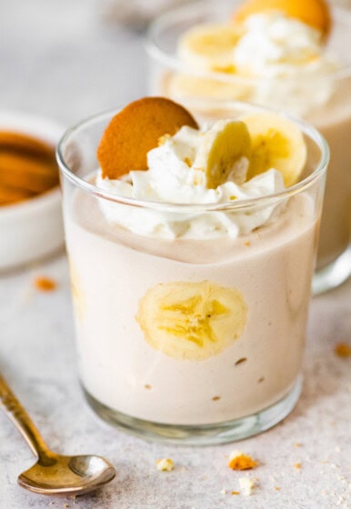 High-protein banana pudding in a glass topped with whipped cream, sliced bananas and a wafer cookie.