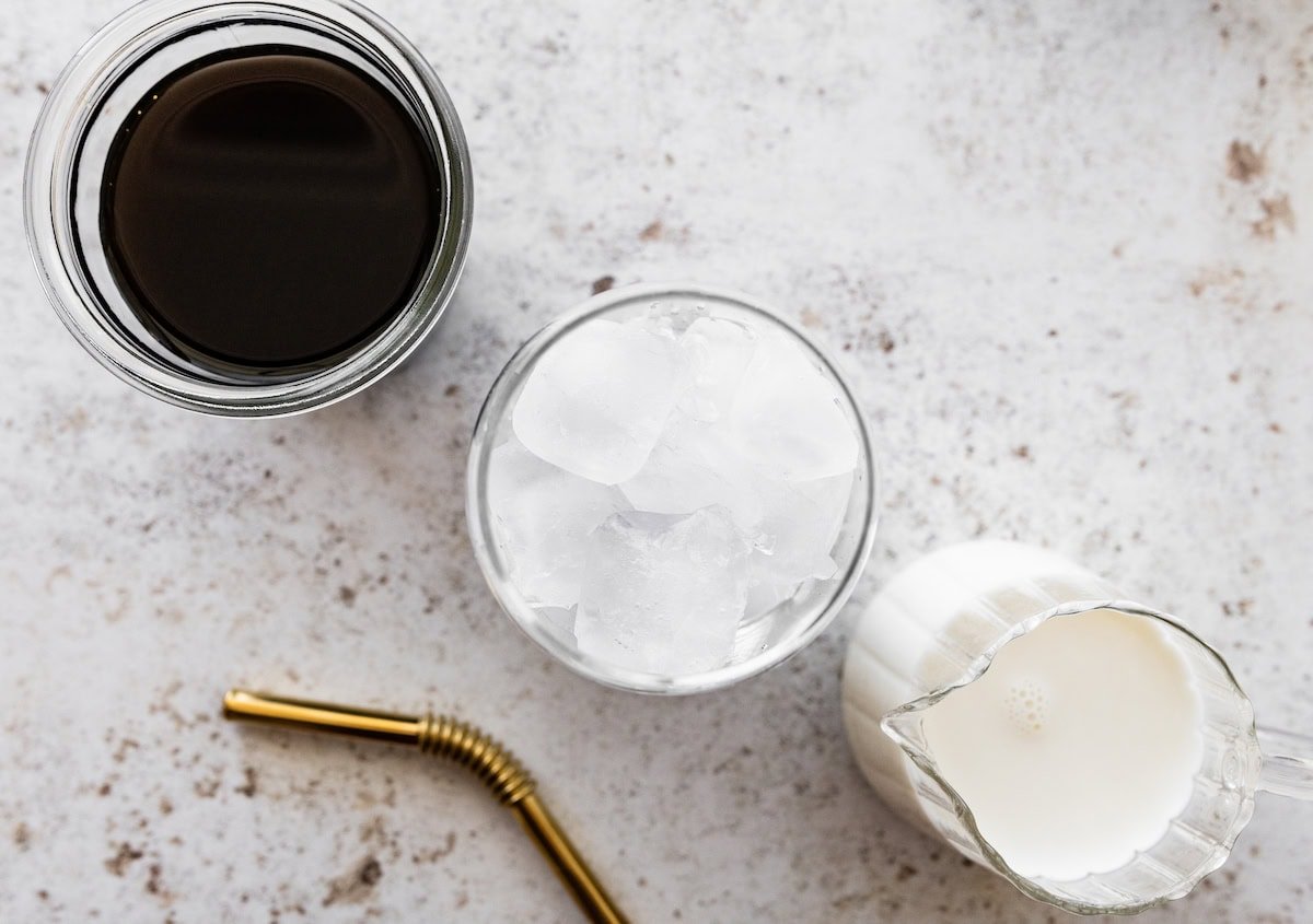 Three glasses—one with black coffee, one with ice, and one with milk—next to a gold metal straw.