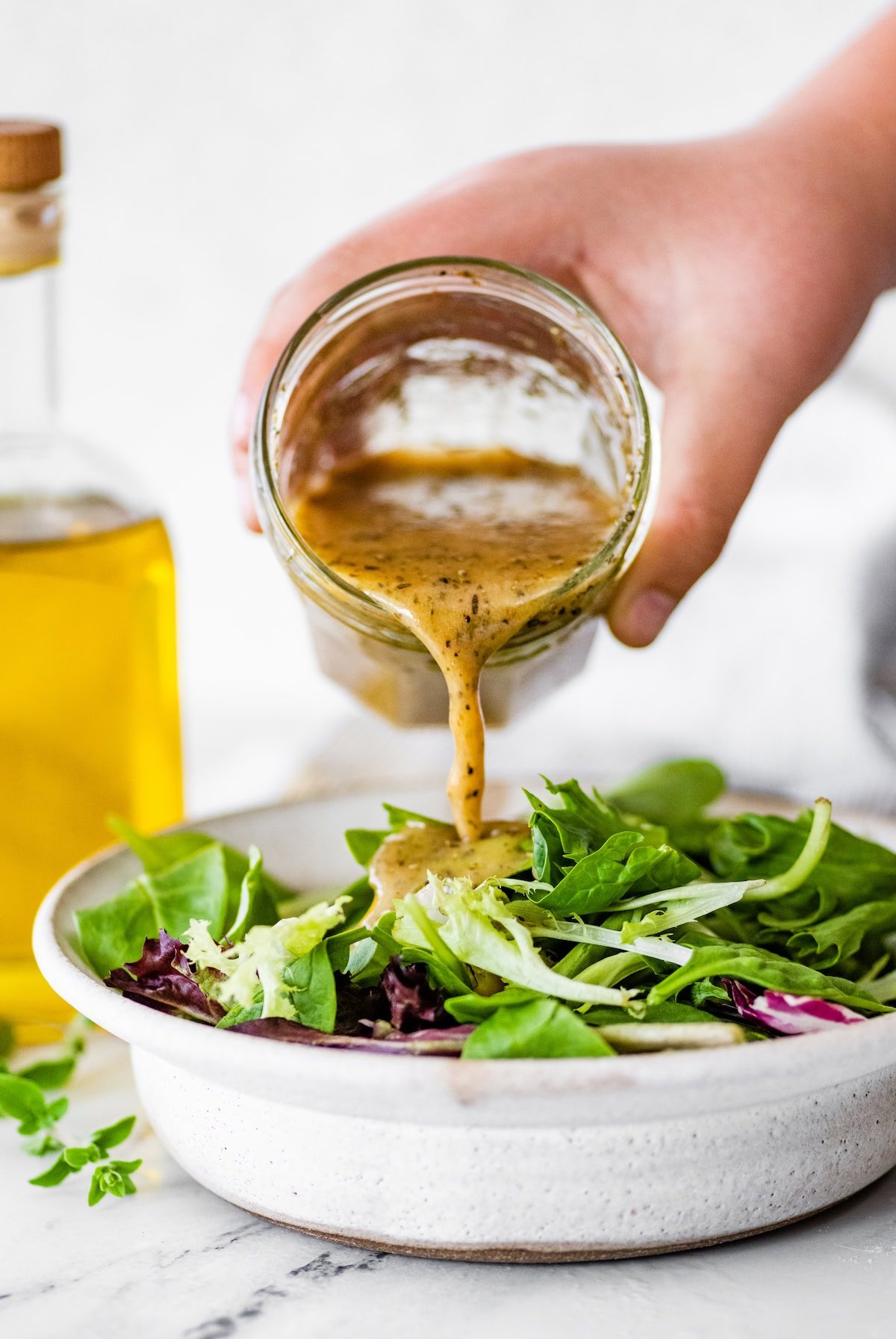Pouring homemade Italian dressing over a fresh green salad.
