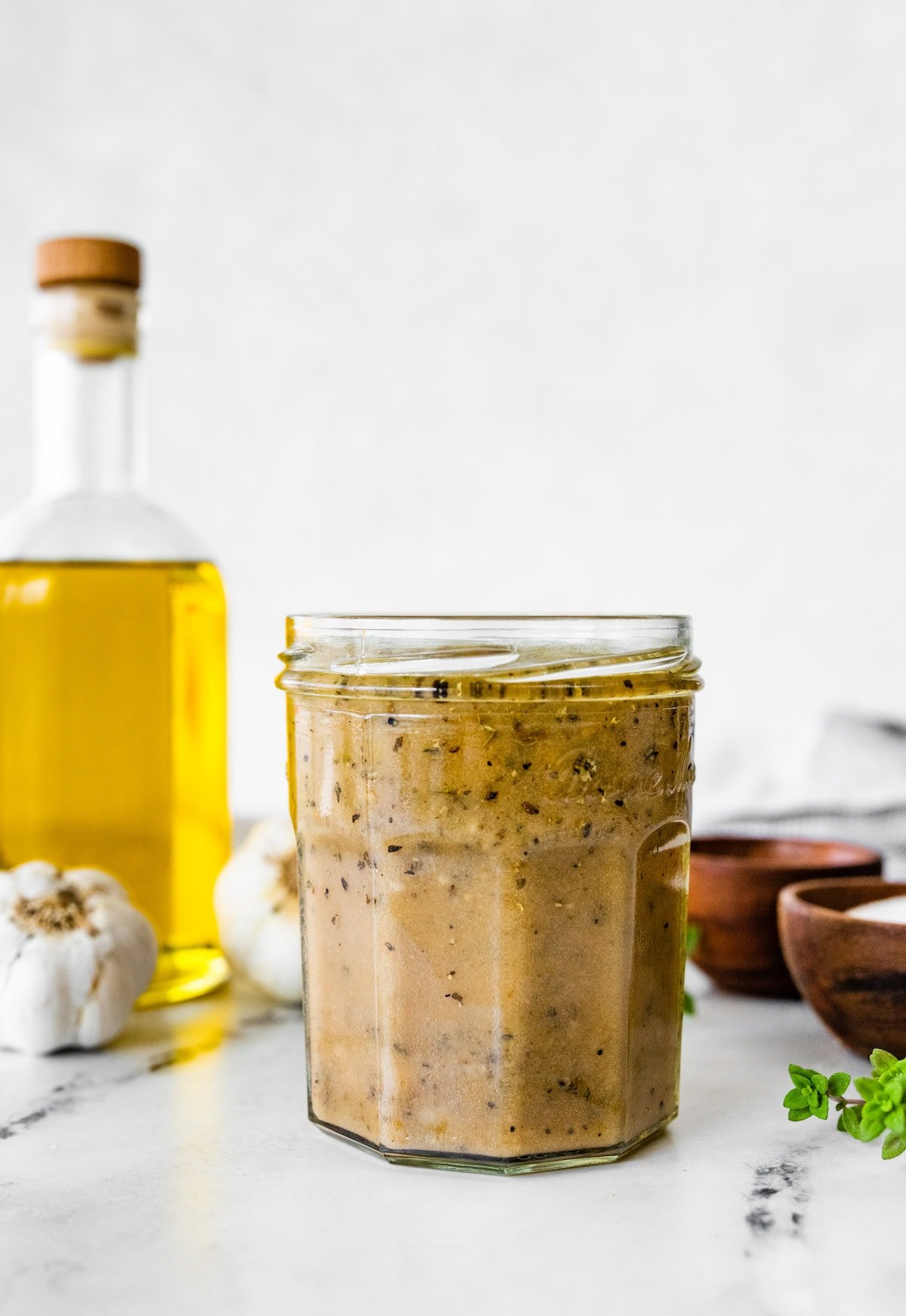 Jar of homemade Italian dressing with olive oil and garlic in the background.