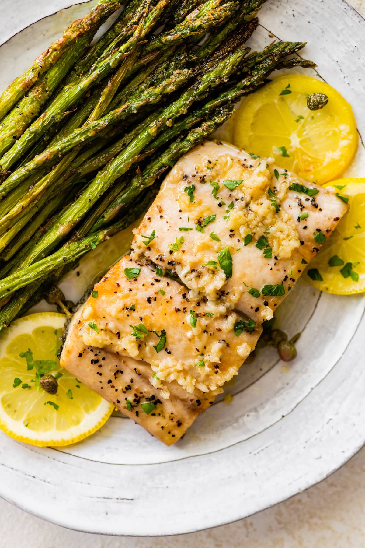 One mahi mahi filet on a plate topped with fresh parsley served with roasted asparagus and lemon slices.
