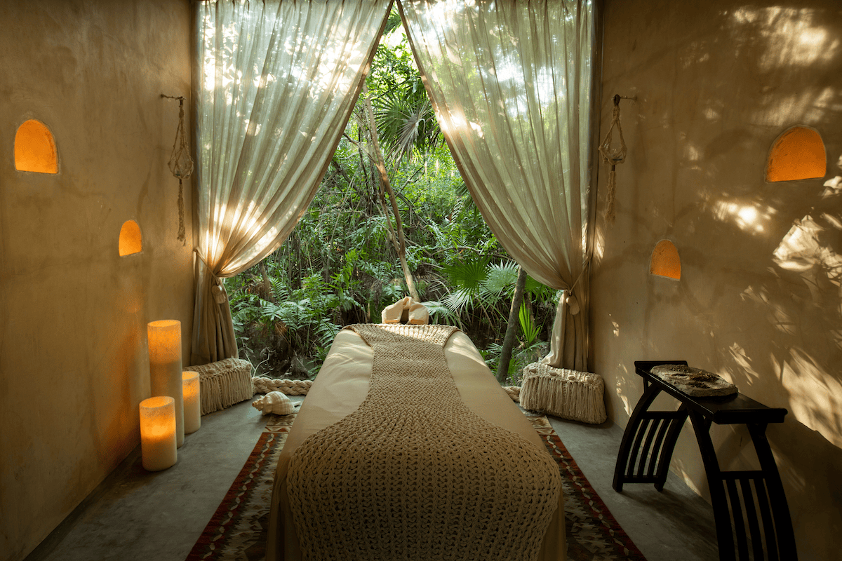 Peaceful jungle spa room with a massage table and flowing curtains open to the greenery outside.
