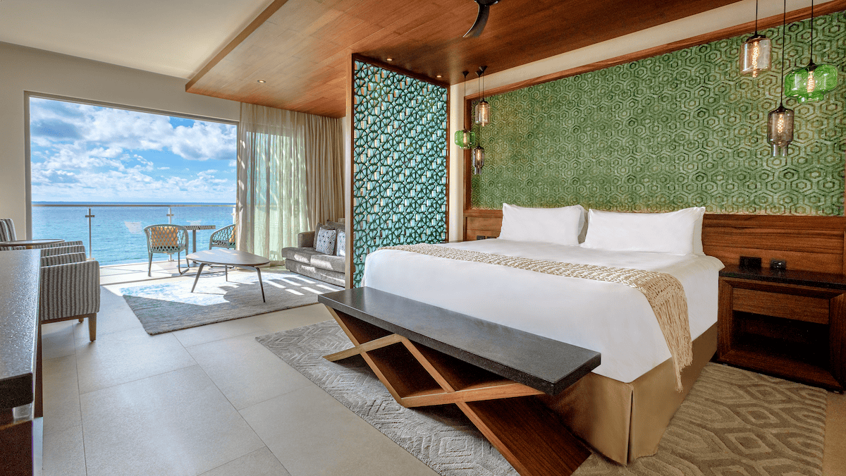 Oceanfront hotel suite with a king bed, sitting area, and private balcony view of the sea.