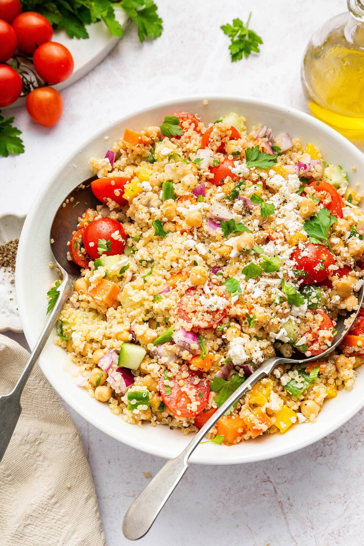 A quinoa chickpea salad in a white bowl with two serving spoons.