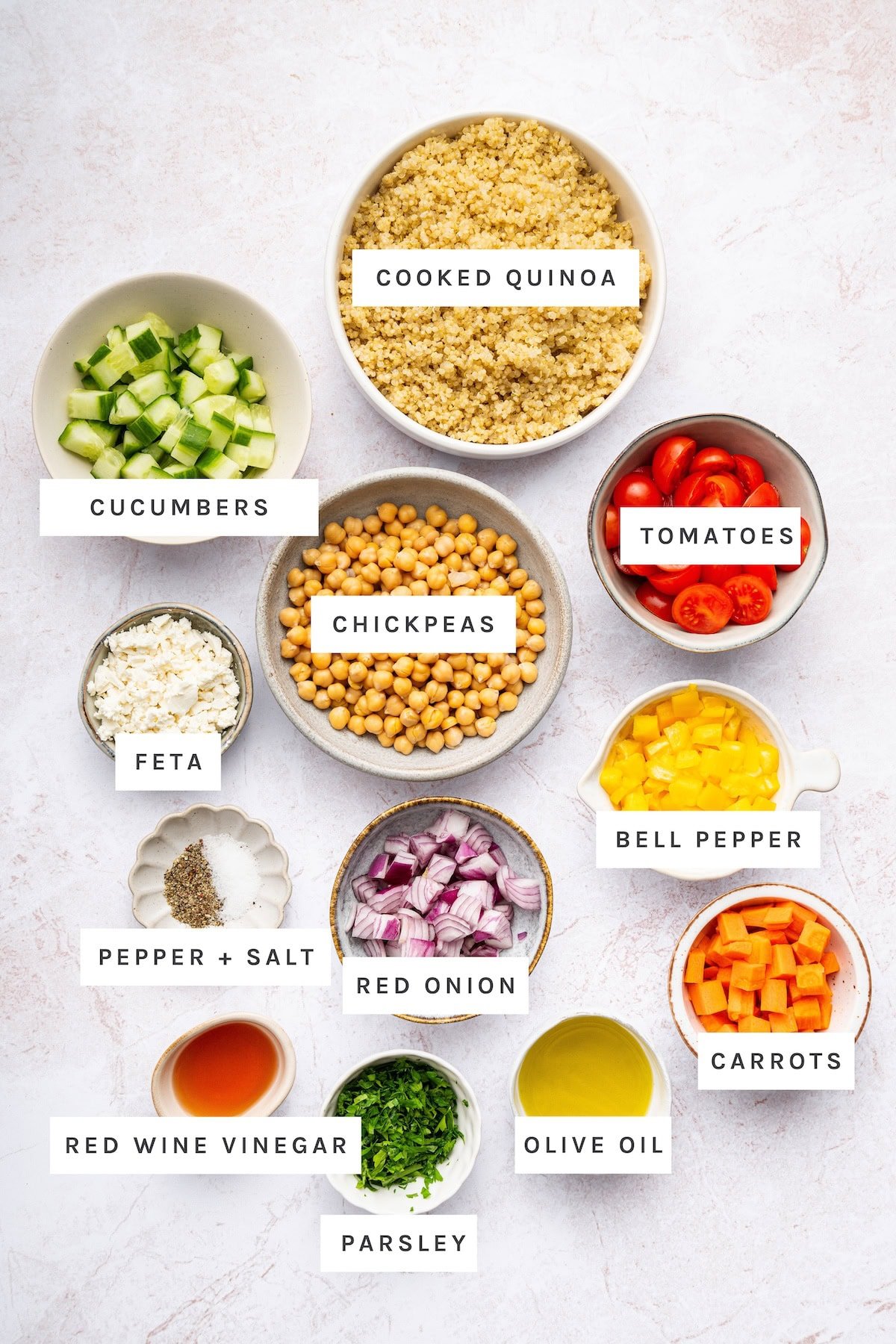 Quinoa Chickpea Salad ingredients: Cooked quinoa, cucumbers, chickpeas, tomatoes, feta, bell pepper, red onion, carrots, red wine vinegar, olive oil, parsley, pepper, salt.