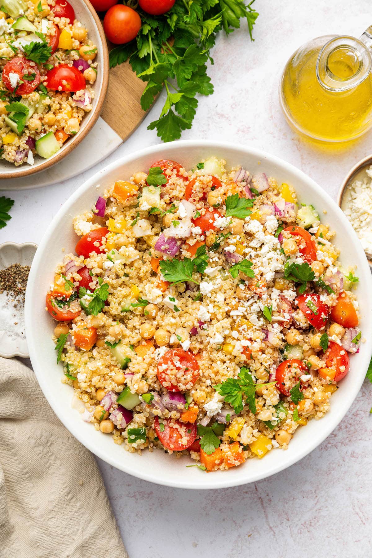 A quinoa chickpea salad in a white bowl with cherry tomatoes, feta cheese, and fresh parsley.