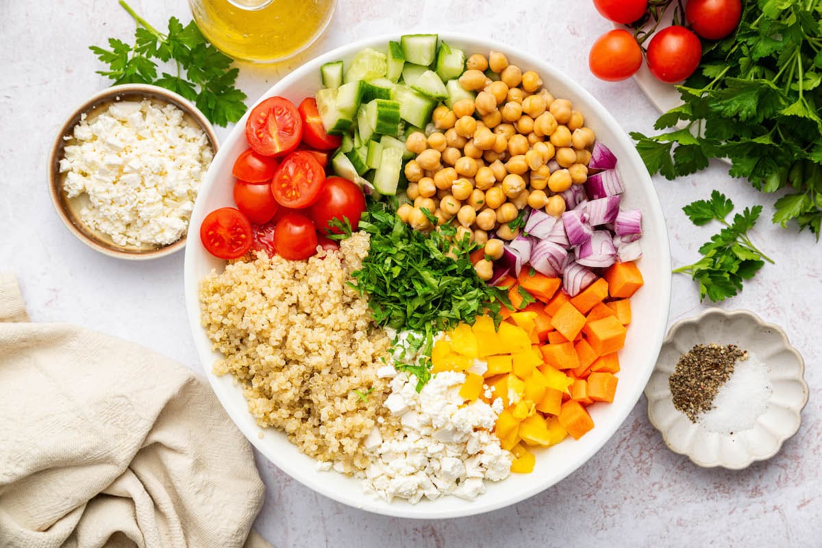 Bowl of salad ingredients like quinoa, chickpeas, tomatoes, and chopped vegetables arranged before mixing.