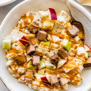 A snickers salad protein bowl topped with apple chunks, a chopped protein bar and a drizzle of peanut butter.