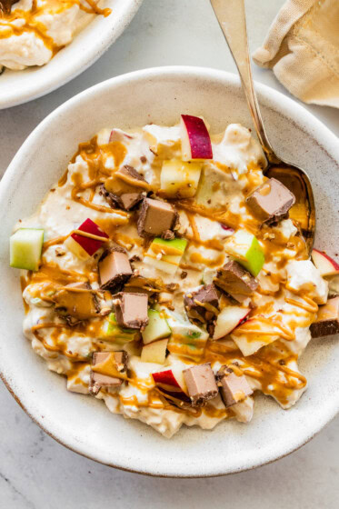 A snickers salad protein bowl topped with apple chunks, a chopped protein bar and a drizzle of peanut butter.