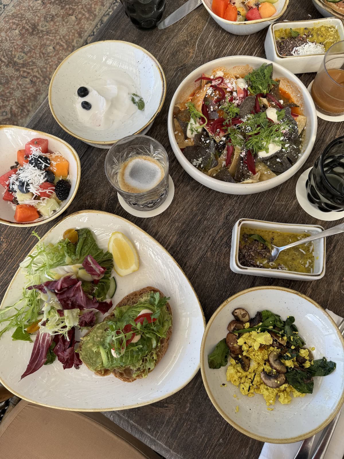 A table filled with fresh breakfast dishes including avocado toast, fruit, and yogurt.