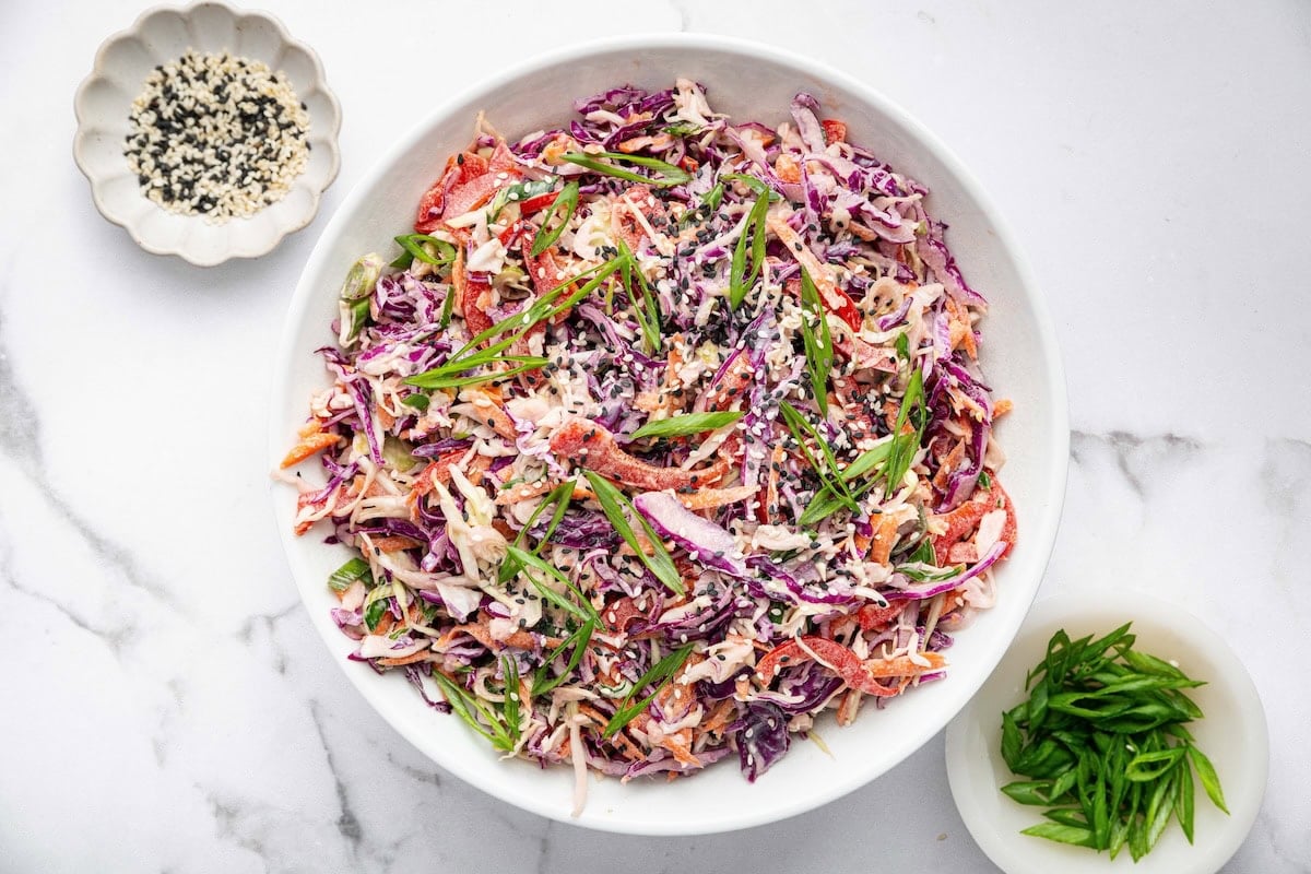 Assembled Asian slaw in a white bowl, garnished with sesame seeds and scallions.