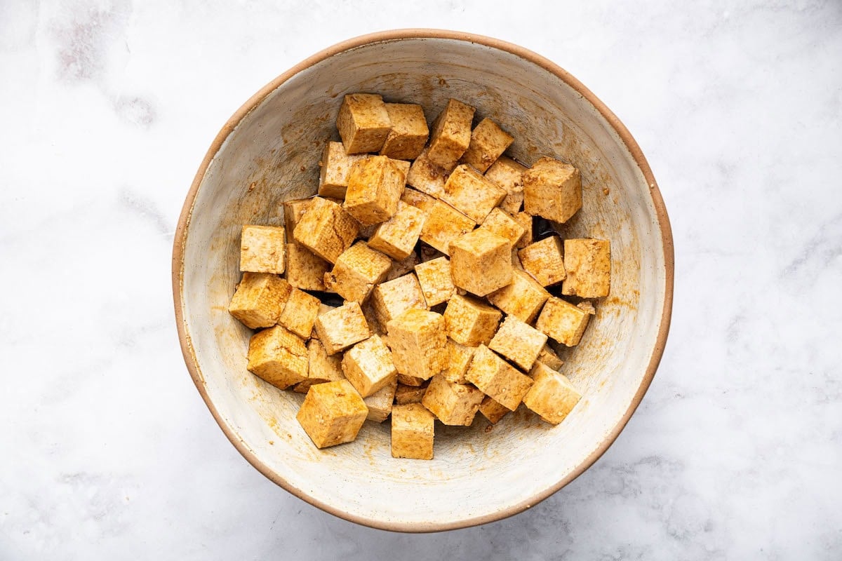 Tofu cubes tossed in marinade inside a mixing bowl, ready for baking.