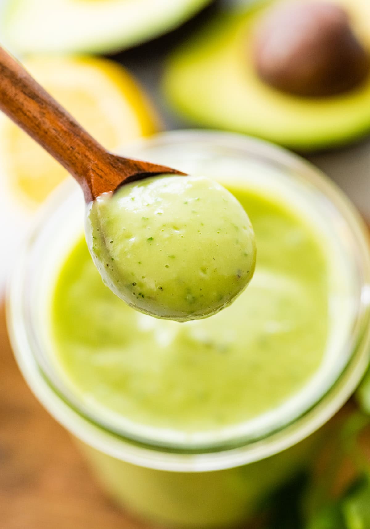 Spoonful of thick avocado dressing held over a bowl.