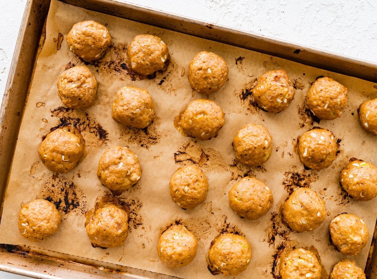 Baked chicken meatballs on a parchment-lined baking sheet.
