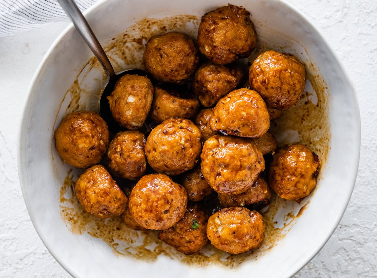 Bowl of BBQ chicken meatballs coated in sauce with a spoon.