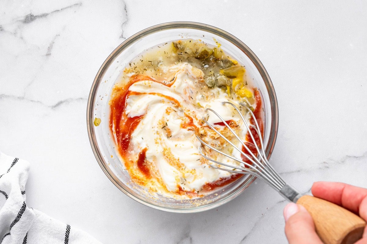 Whisk mixing ingredients like pickles, ketchup, and mayo in a glass bowl to make Big Mac sauce
