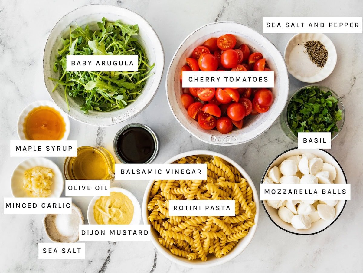 Caprese Pasta Salad ingredients: Baby arugula, cherry tomatoes, sea salt and pepper, maple syrup, balsamic vinegar, minced garlic, olive oil, rotini pasta, basil, mozzarella balls, dijon mustard, sea salt.