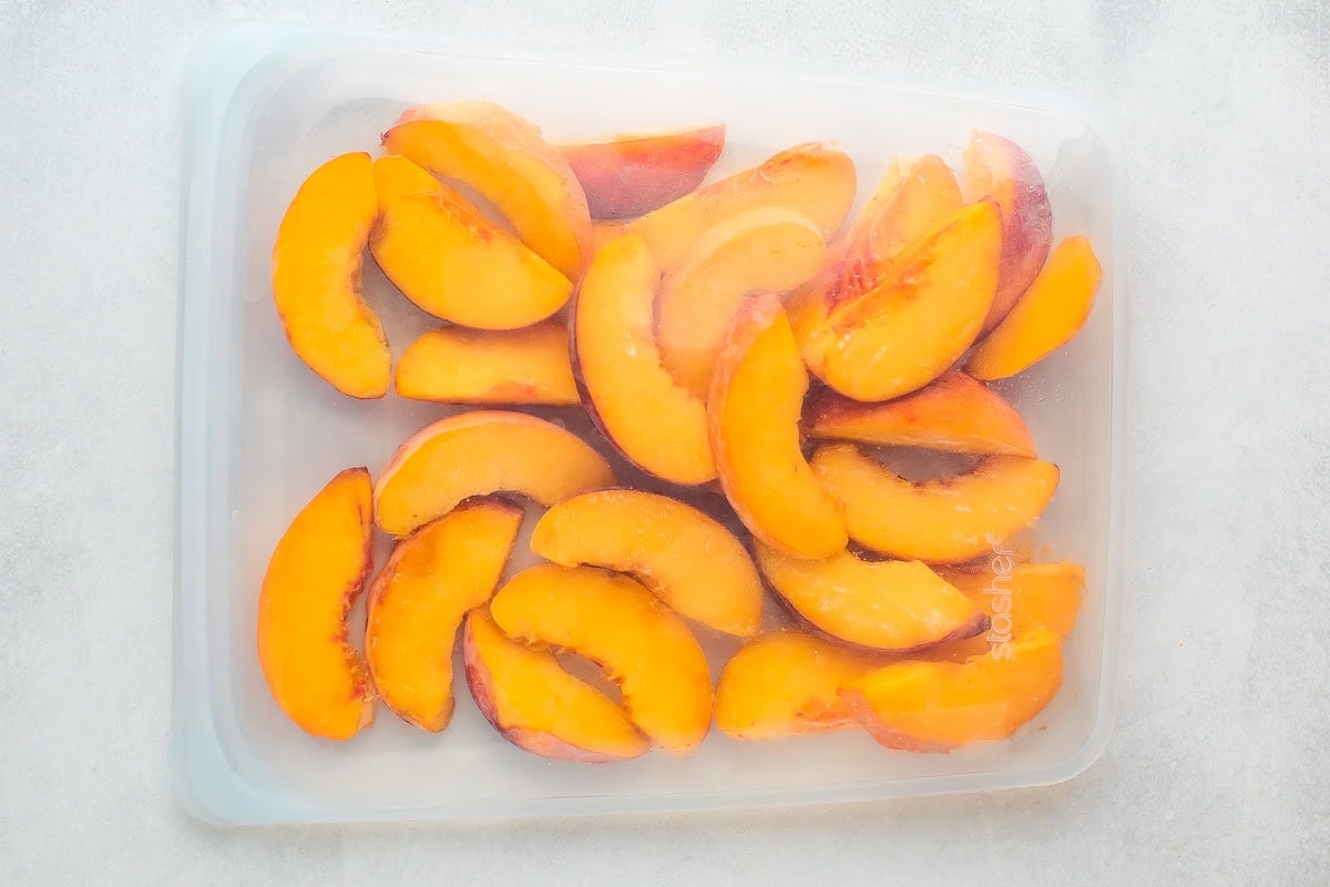 A plastic container filled with sliced peaches.