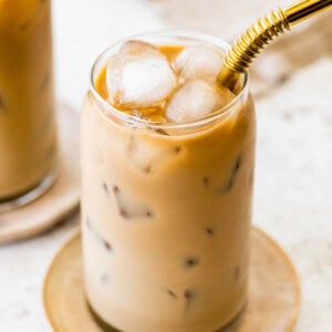 Finished iced coffee with a creamy light brown color and ice cubes, served with a gold metal straw.