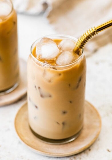 Finished iced coffee with a creamy light brown color and ice cubes, served with a gold metal straw.