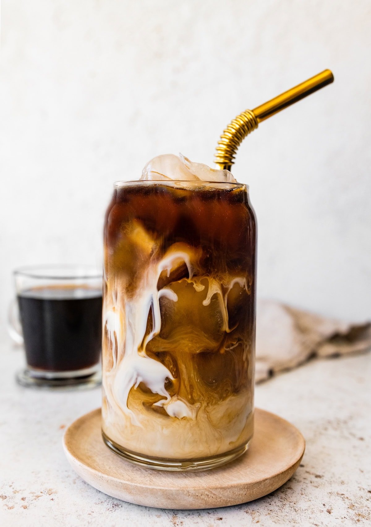 A glass of iced coffee with dramatic milk swirls throughout, topped with ice and a gold straw.