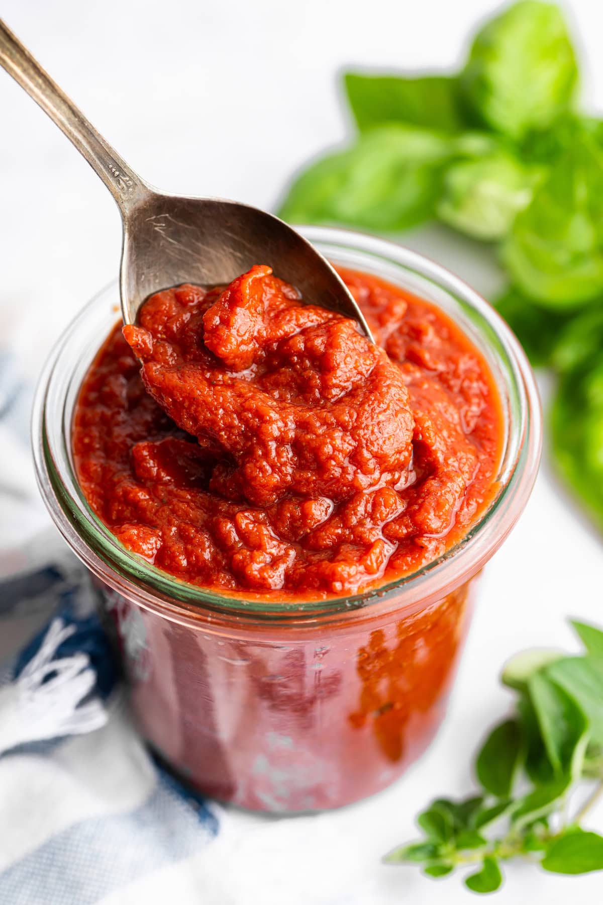 Spoonful of thick homemade pizza sauce being lifted from a glass jar.