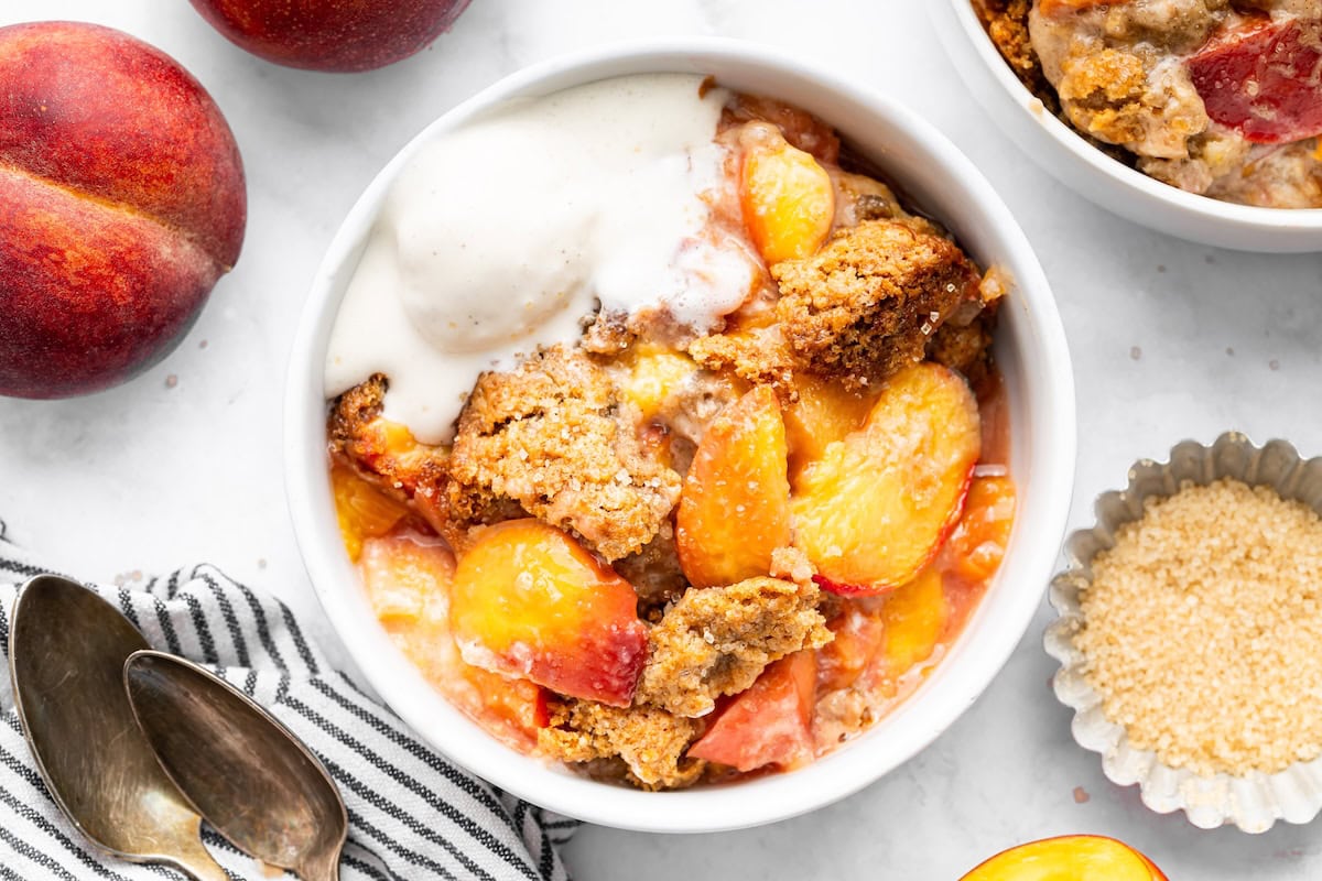 Close-up of a bowl of healthy peach cobbler with golden topping and juicy peaches, served with a scoop of vanilla ice cream.