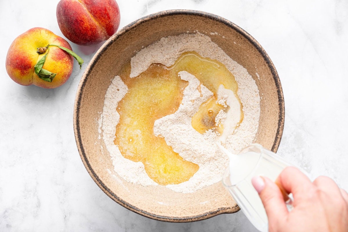 Mixing bowl with melted butter and wet ingredients being poured into dry ingredients to make the cobbler topping.