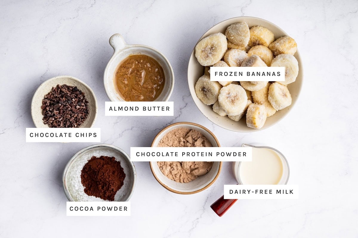 High-Protein Ice Cream ingredients: Frozen bananas, almond butter, chocolate chips, cocoa powder, chocolate protein powder, dairy-free milk.