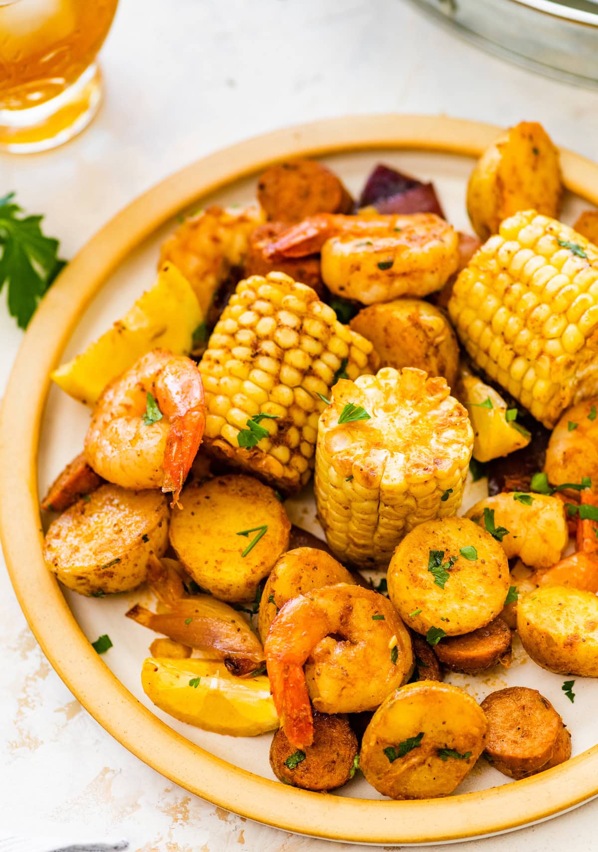 Plate of shrimp boil served with shrimp, corn on the cob, potatoes, and sausage slices.