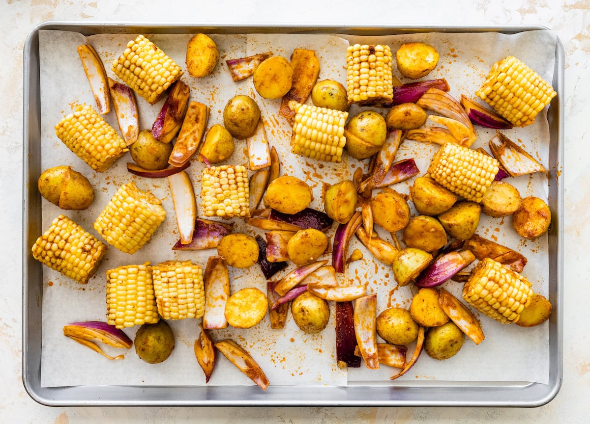 Corn, onions, and potatoes arranged on a baking sheet before roasting