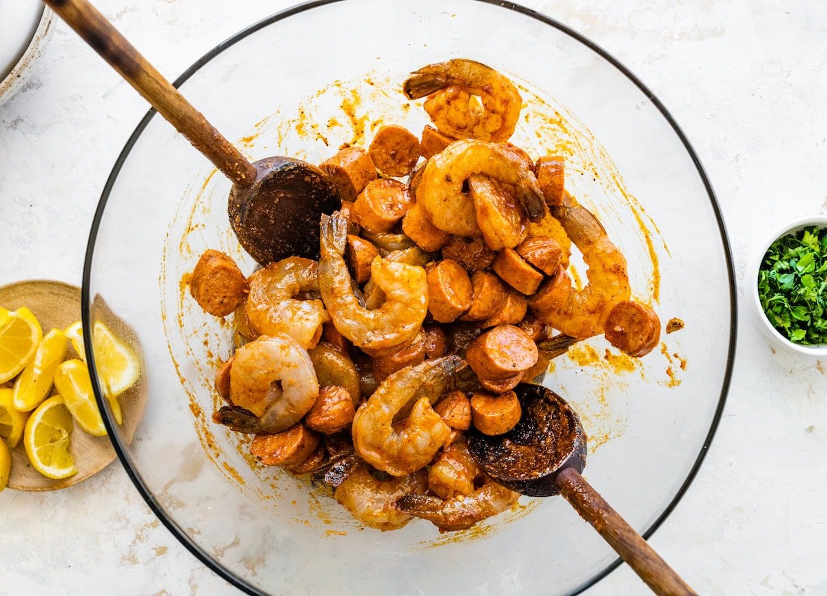 Shrimp, sausage, and onions tossed in seasoned butter mixture in a large mixing bowl.