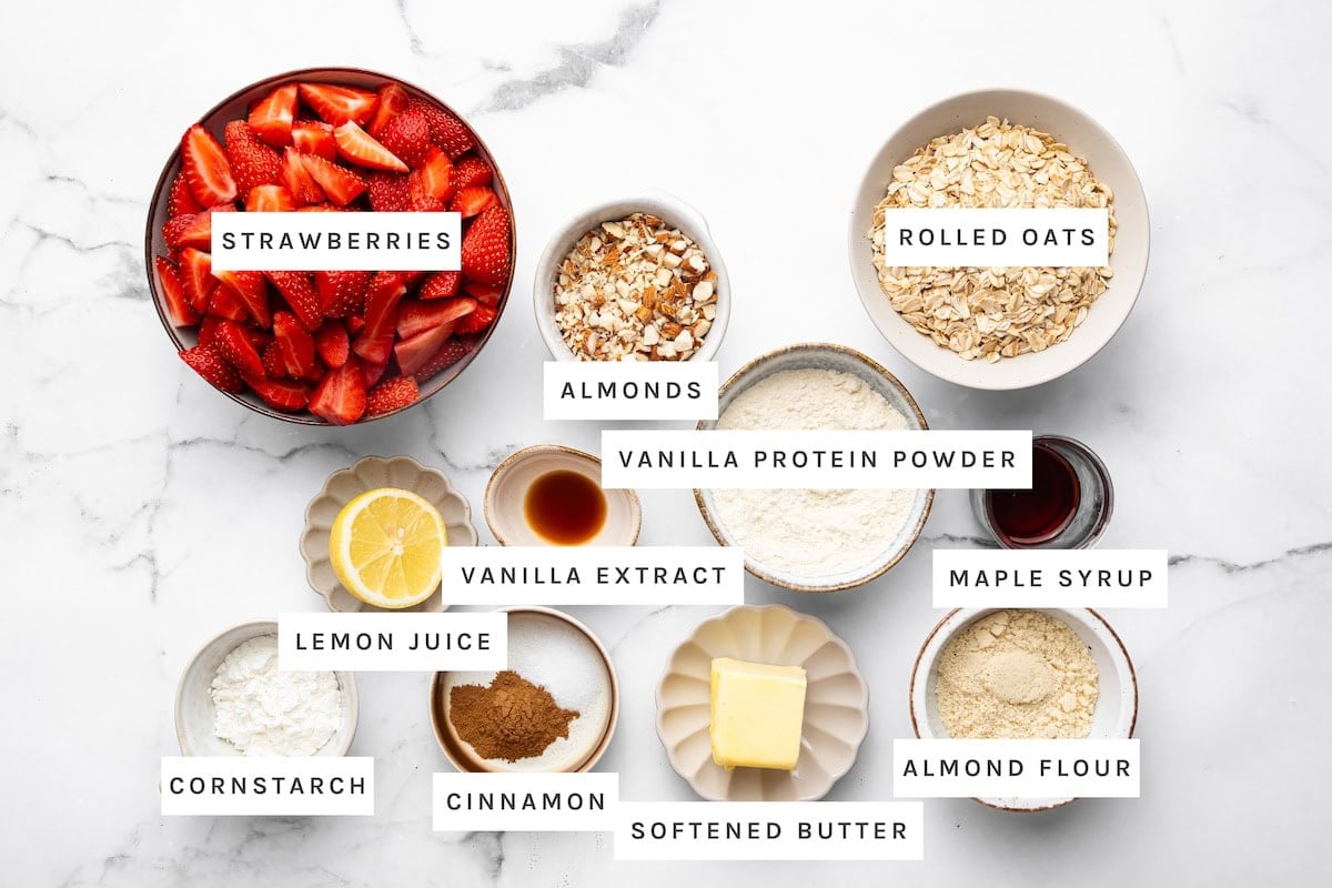 High-Protein Strawberry Crisp ingredients: Strawberries, almonds, rolled oats, vanilla protein powder, maple syrup, vanilla extract, lemon juice, cornstarch, cinnamon, softened butter, almond flour.