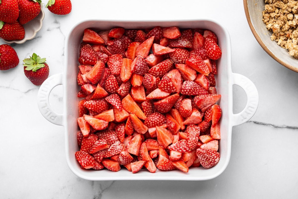 The strawberry slices tossed with arrowroot powder in a square white baking dish.